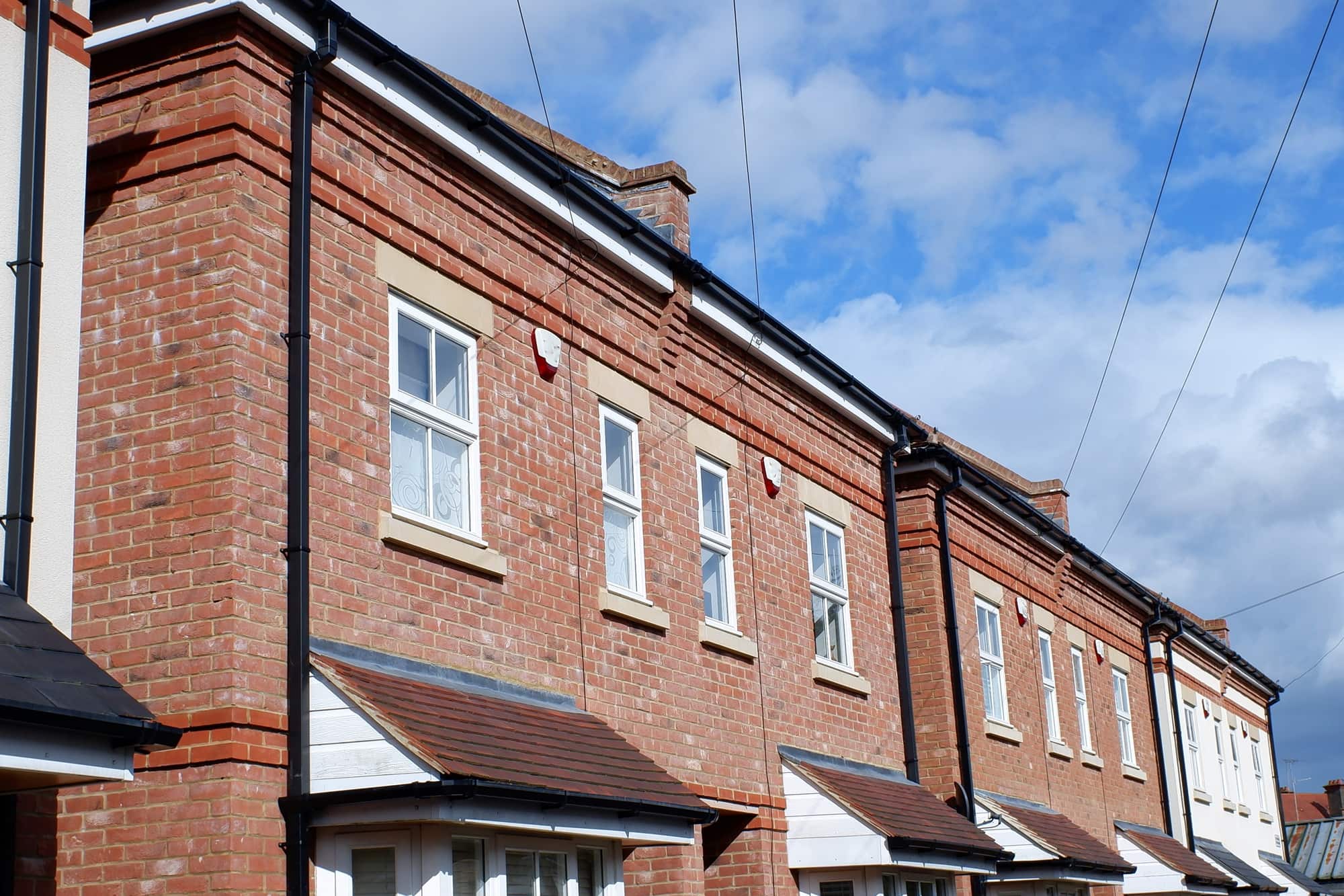 Red-brick terraced houses with white windows beneath a blue sky.