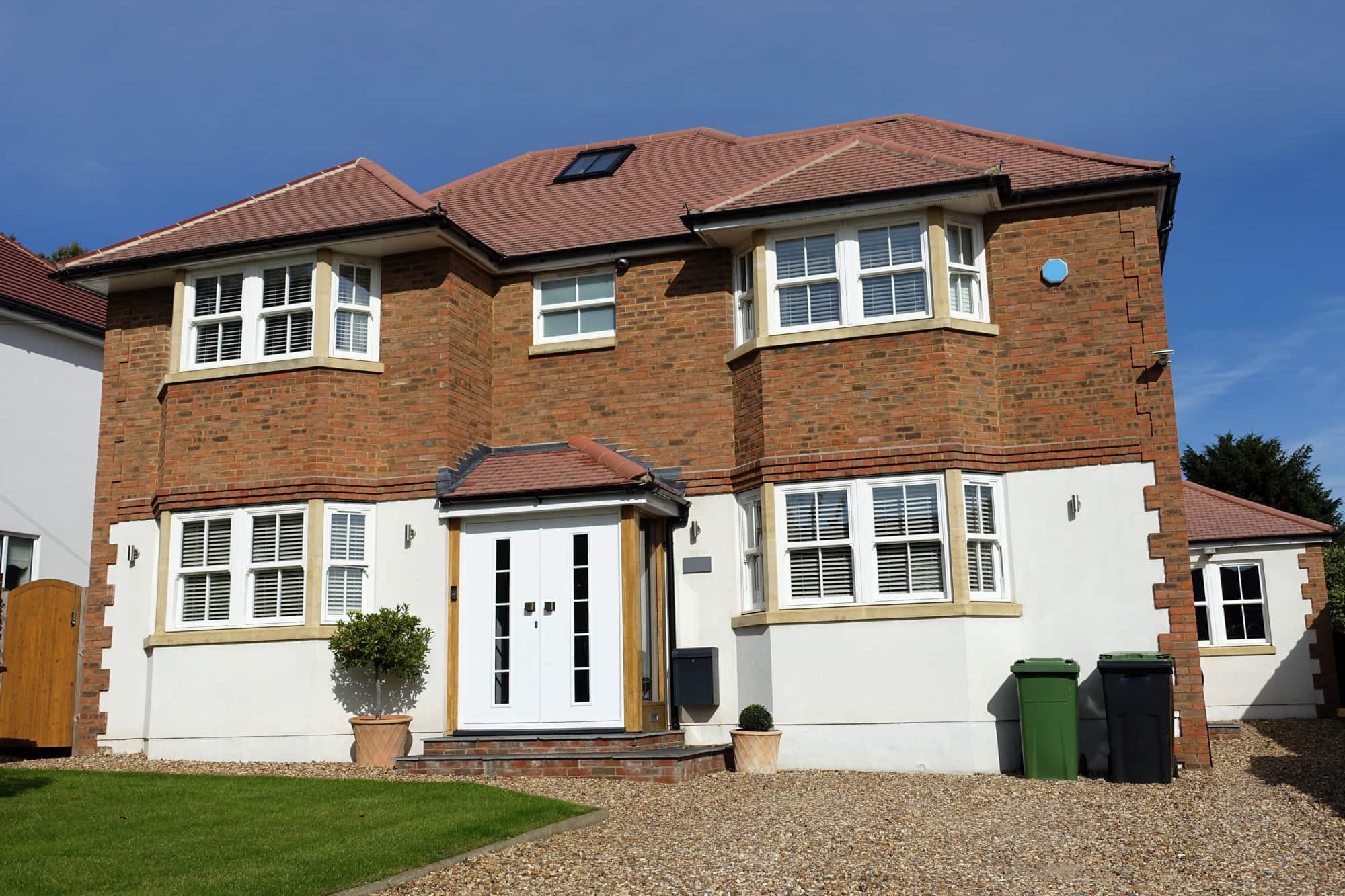 Detached brick and white-rendered house with bay windows and a gravel driveway.